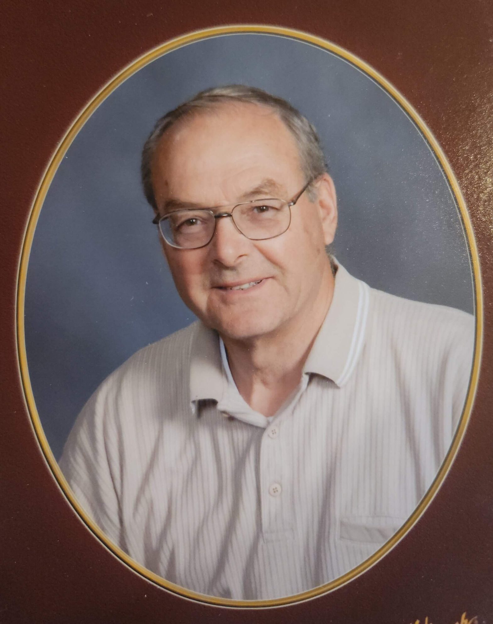 Oval-framed portrait of an older man wearing glasses and a light striped shirt, smiling.