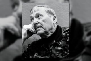 Black-and-white portrait of an older man with a contemplative expression, resting his chin on his hand.