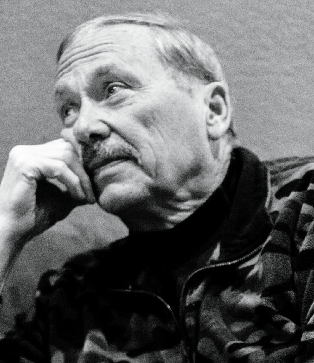 Black-and-white portrait of an older man with a contemplative expression, resting his chin on his hand.